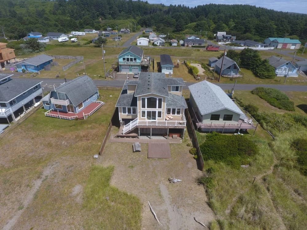 Tan two-story house with white-railed deck and picnic table in Moclips