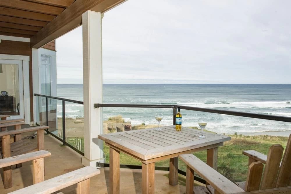 Wooden table and benches on a glass-railed deck facing ocean in Newport