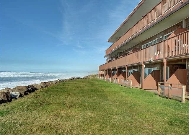 Brown three-story condo with wooden balconies beside rocky shore in Neskowin