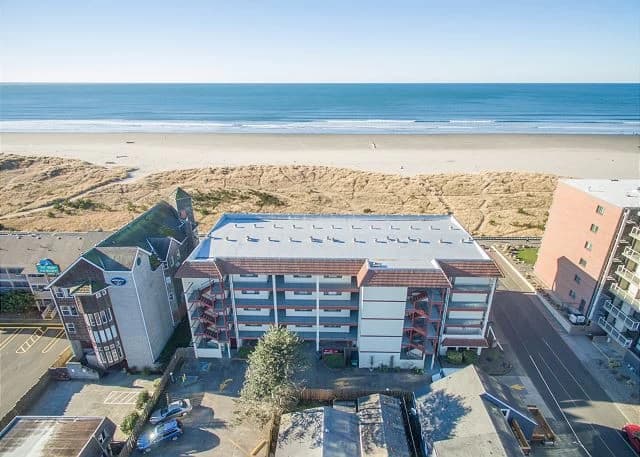 White oceanfront condo in Seaside with balconies, red stairs, and a wide sandy beach