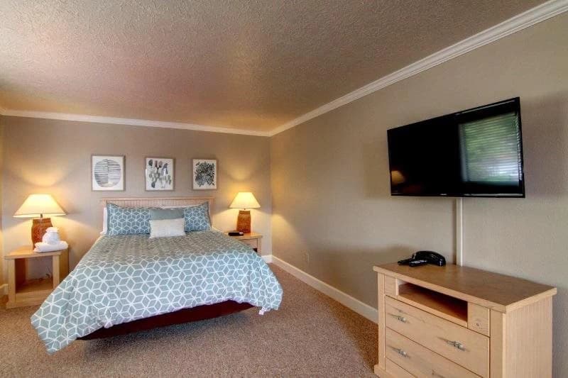 Cannon Beach bedroom with a blue patterned duvet, botanical prints, and wall-mounted TV