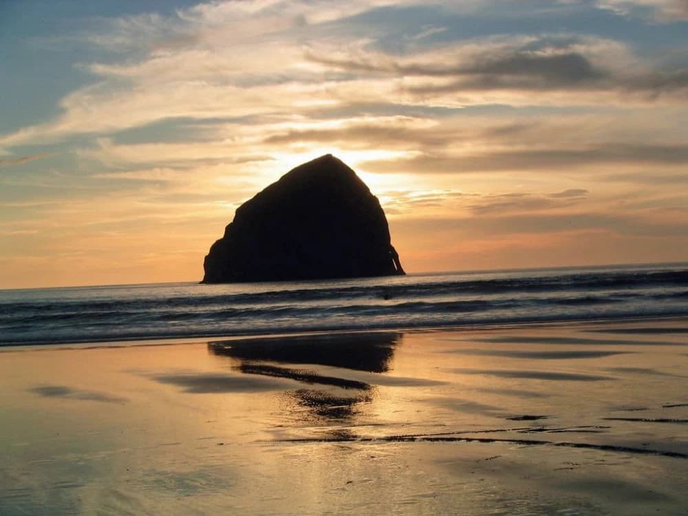 Sea stack silhouetted at sunset on a wet sandy beach in Pacific City with glowing sky