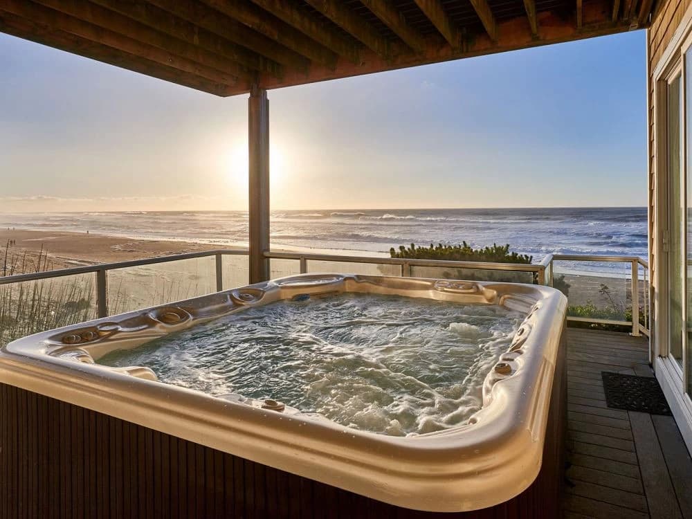 Hot tub on a wood deck in Gleneden Beach with glass railing overlooking beach and sunset