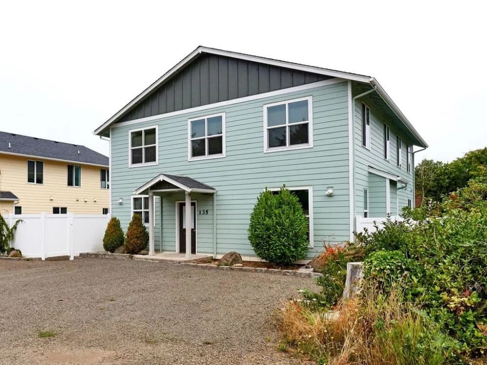 Seafoam-green house in Lincoln Beach with a gray gable, white porch pillars, and gravel drive