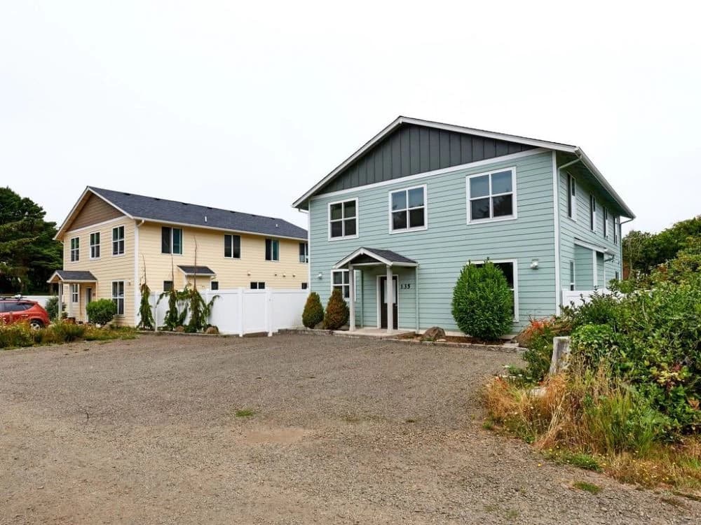 Seafoam-green two-story house in Lincoln Beach with a gravel drive and gabled porch