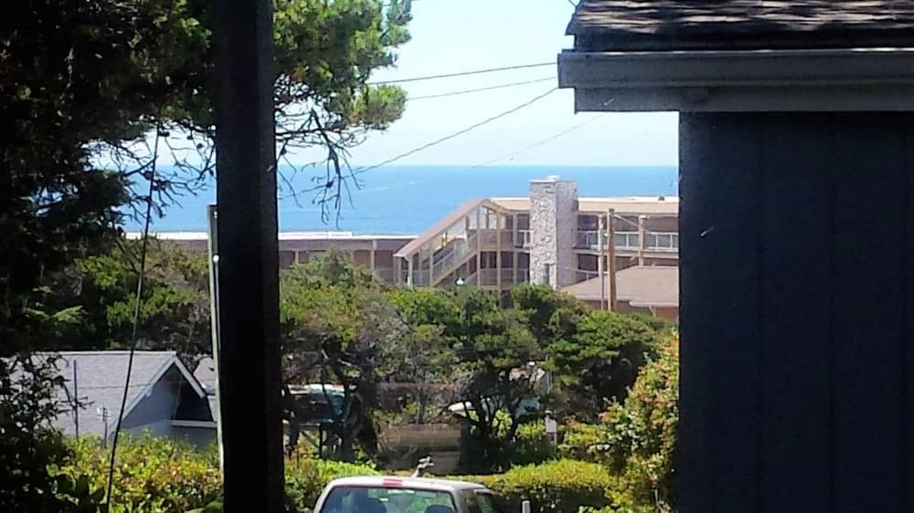 Distant ocean view in Florence framed by trees, a tan condo, and a parked car