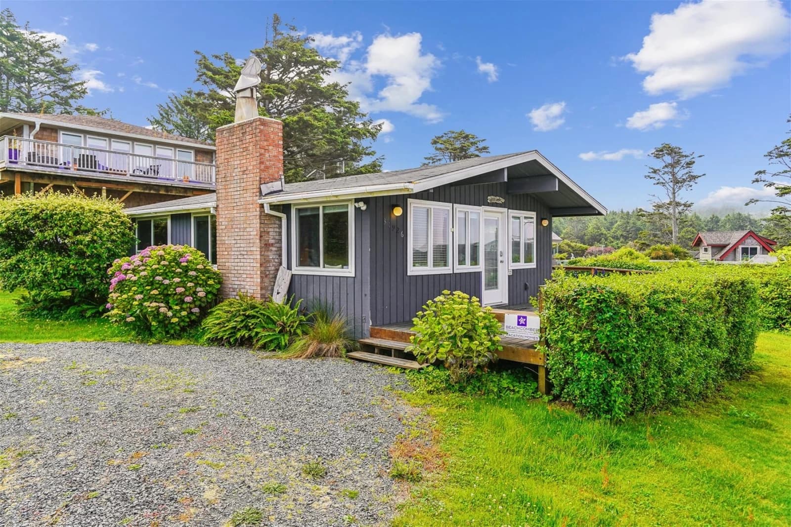 Dark slate-blue cottage in Arch Cape with a red brick chimney and hydrangea bushes