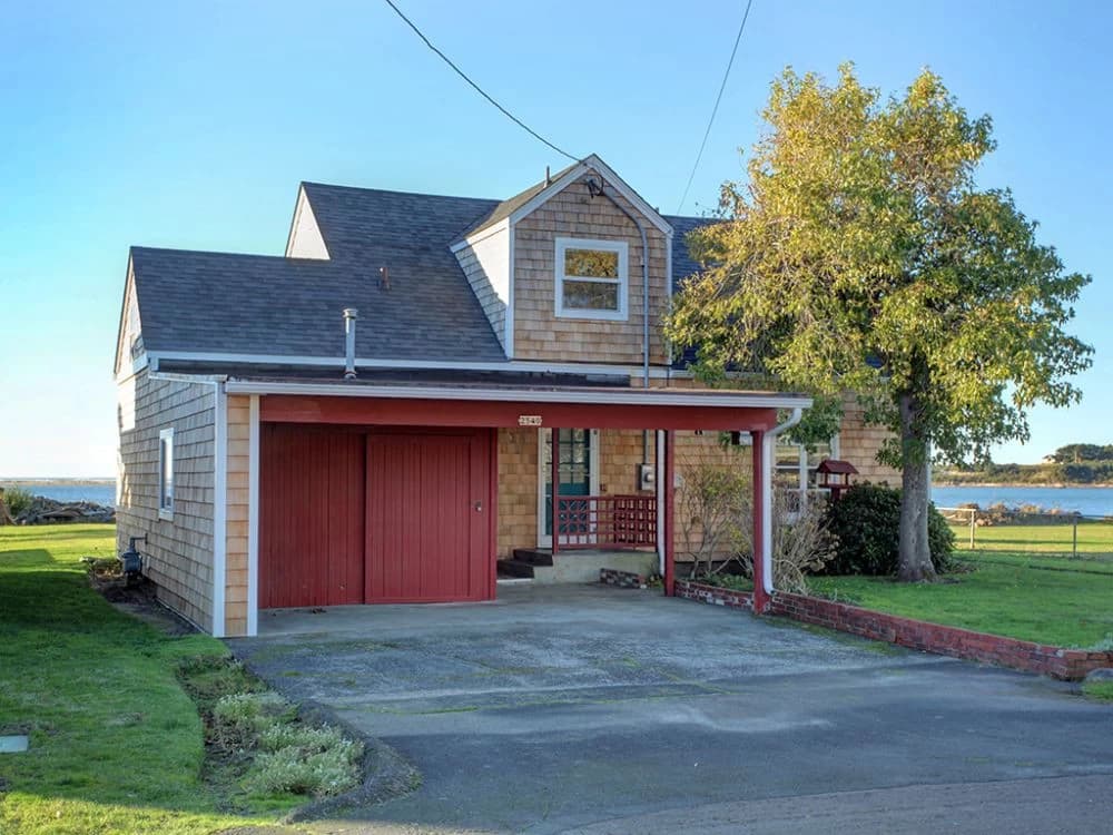 Cedar-shingle cottage in Seaside with a red carport and blue water behind the lawn