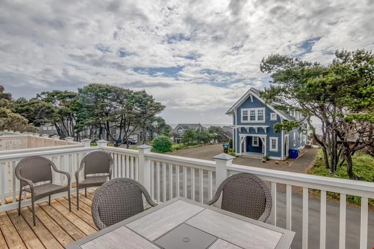 Deck dining set overlooking a blue house, trees, and ocean in Depoe Bay