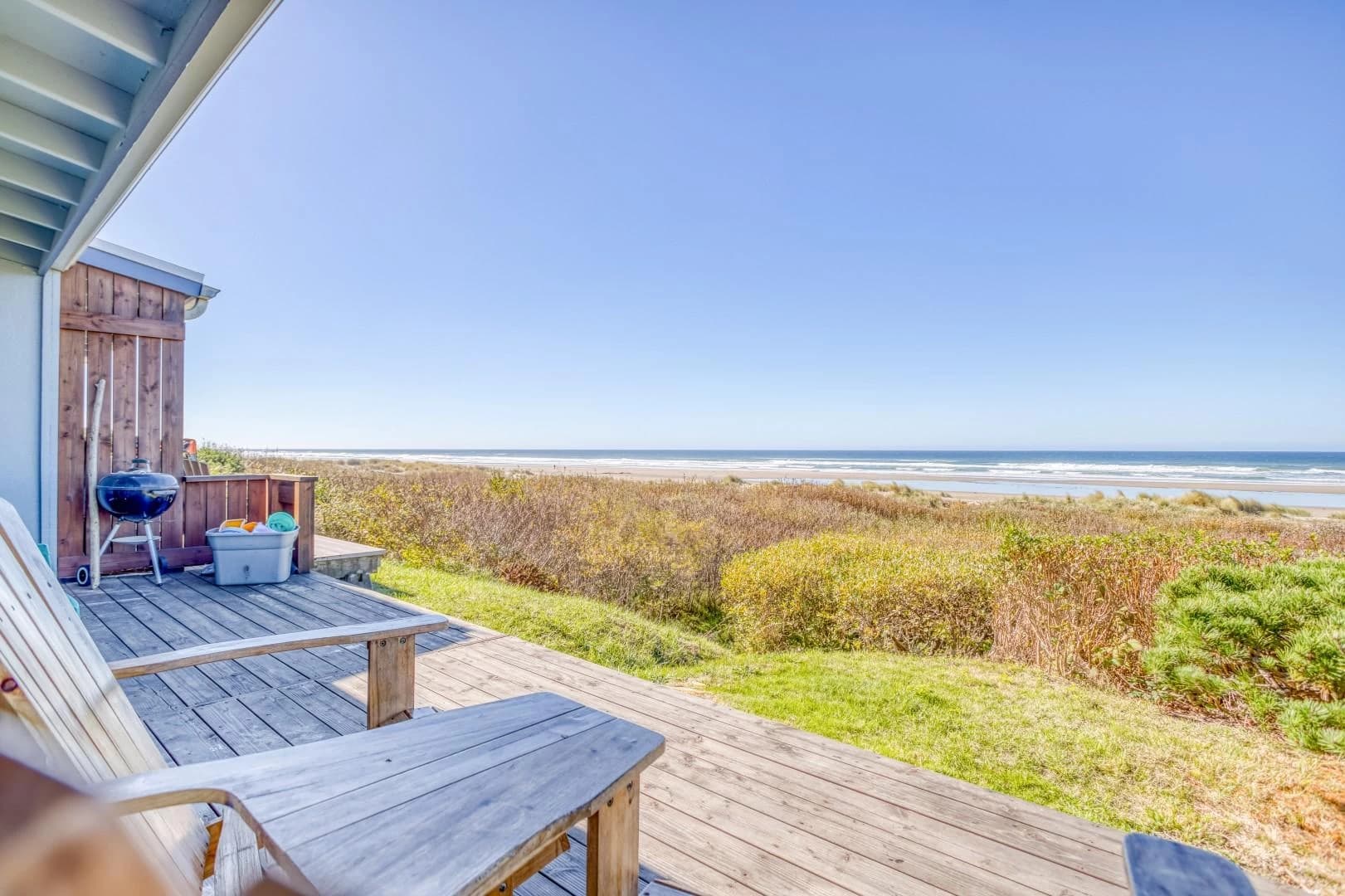Weathered wooden deck with a blue grill overlooking beach and ocean in Waldport
