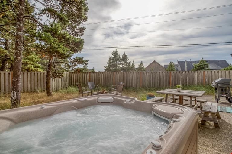 Beige bubbling hot tub and picnic table in a fenced backyard in Pacific City