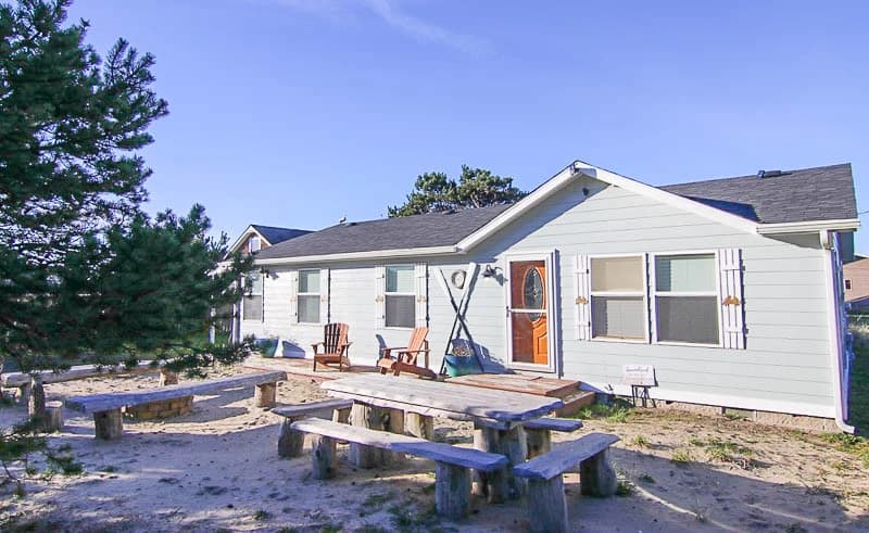 Light blue Waldport cottage with a rustic log picnic table and Adirondack chairs