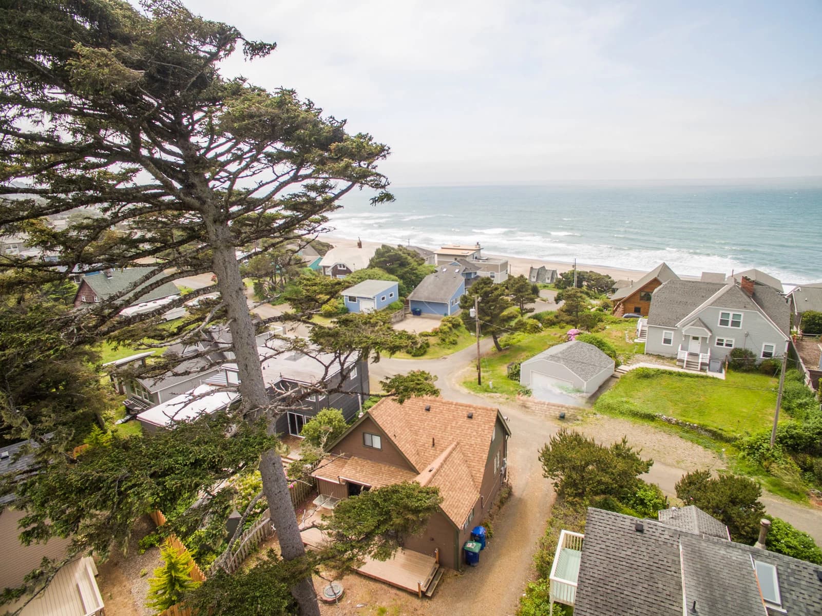 Aerial of a Depoe Bay neighborhood with brown and gray houses, beach, and ocean beyond