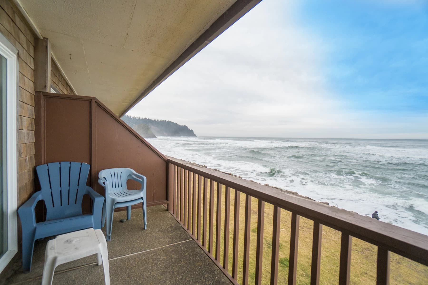 Neskowin balcony with a blue Adirondack chair, wood railing, and ocean waves toward a forested headland
