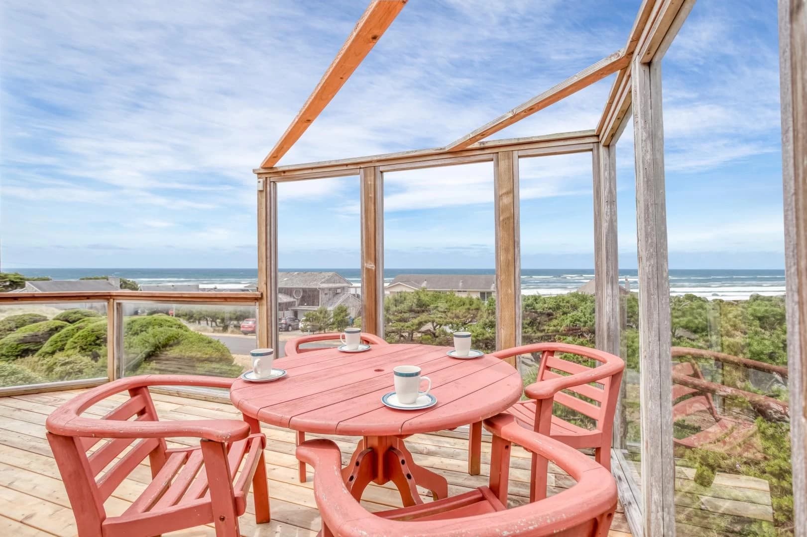 Round coral table with four white mugs on a Waldport deck overlooking the ocean