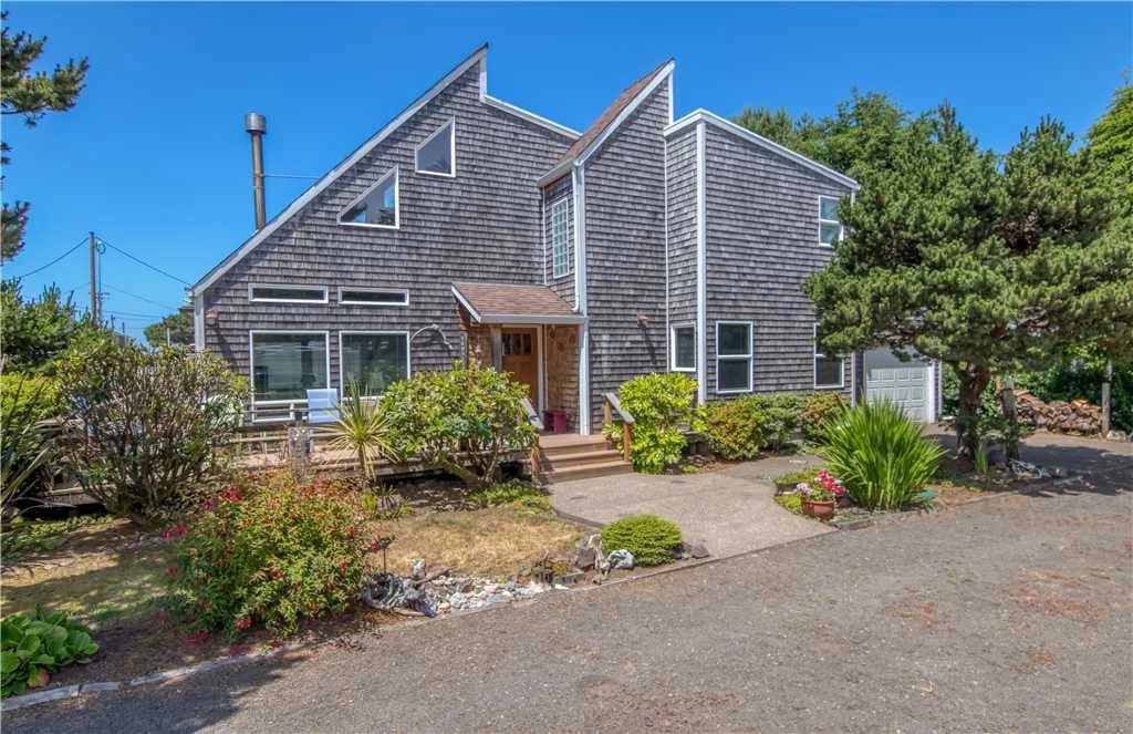 Gray cedar-shingle Neskowin house with angular gables, white trim, and a front walk