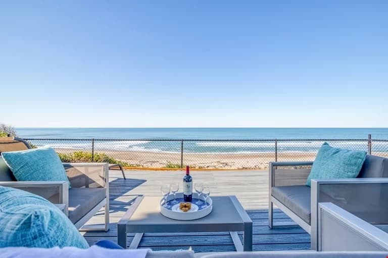 Gray deck in Lincoln City with teal-pillow chairs, wine glasses, and an ocean view