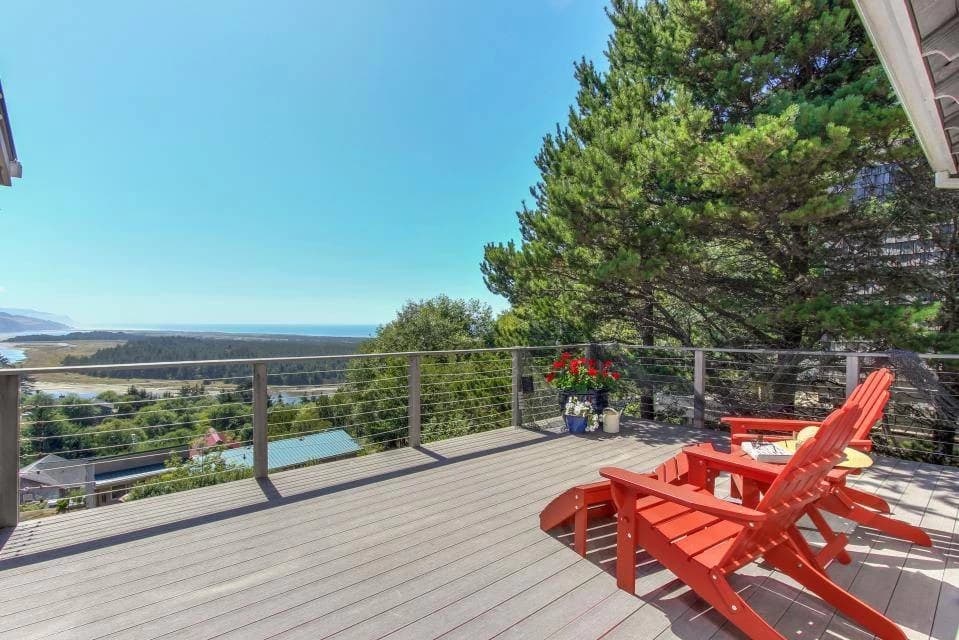 Two red Adirondack chairs on a cable-rail deck overlooking ocean in Pacific City