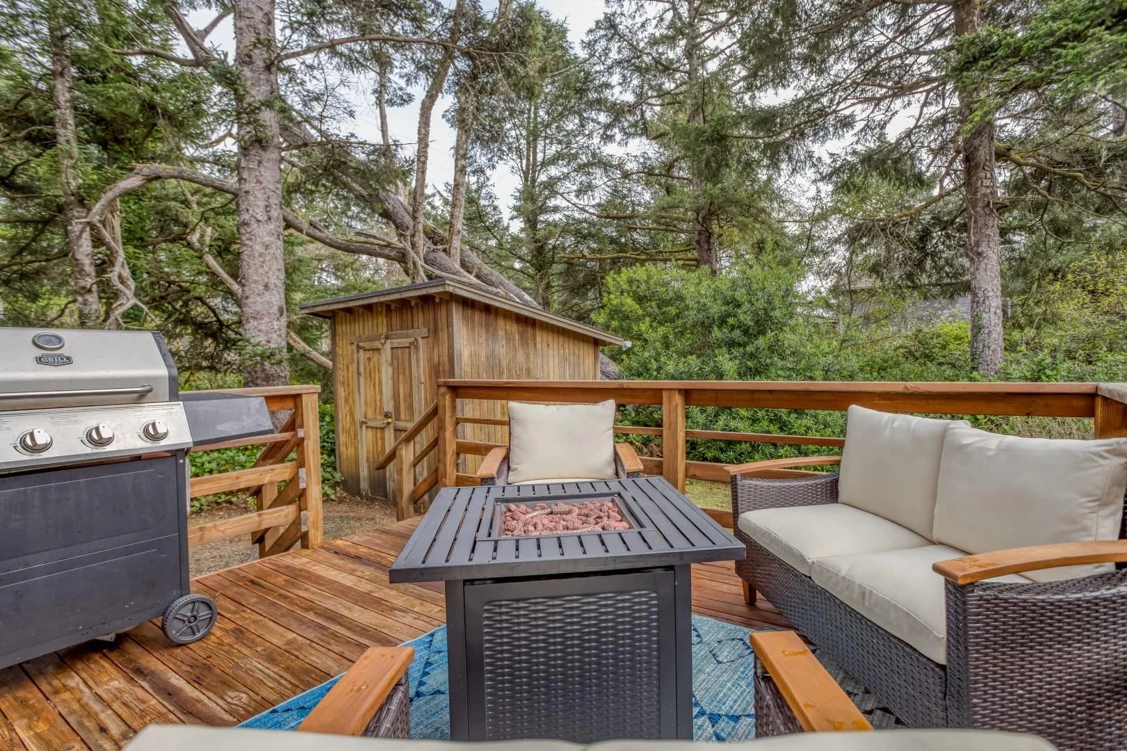 Wood deck in Manzanita with wicker seating, fire pit table, and grill among trees