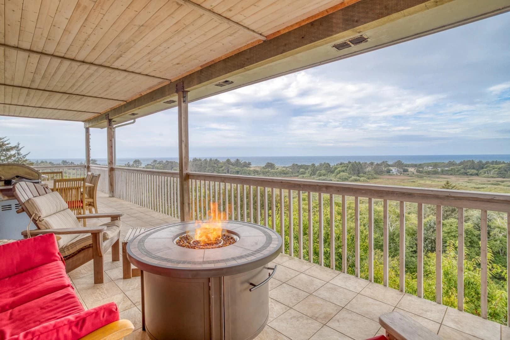 Covered deck in Neskowin with a fire pit, red cushions, and distant ocean view