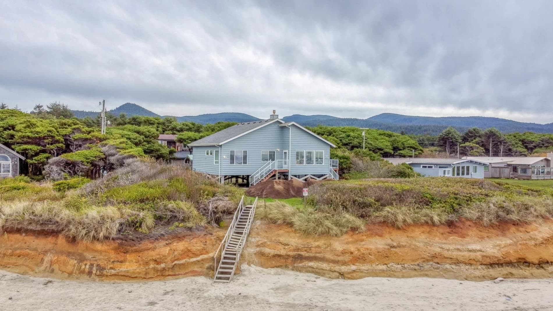 Light-blue house on a Yachats bluff with a deck and stairs down to the sandy beach