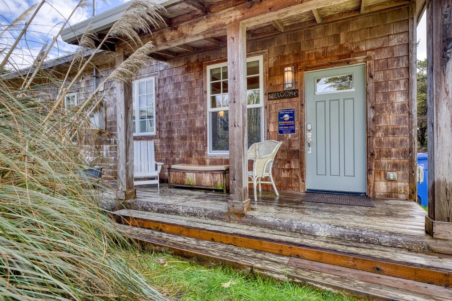 Cedar-shingle cottage in Tierra Del Mar with a seafoam door, porch chairs, and dune grass