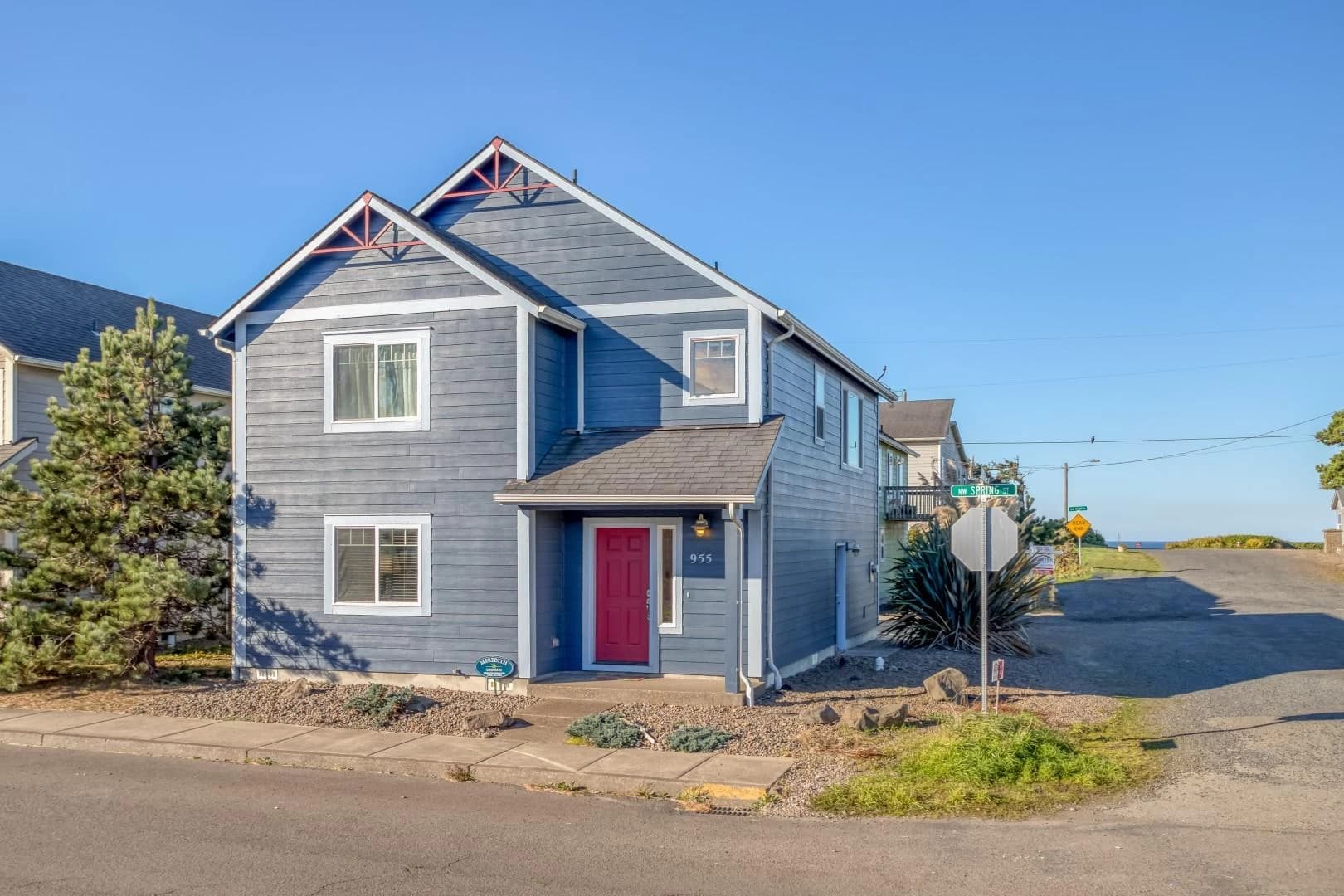 Slate-blue Newport house with a red door, white trim, and gravel on a corner lot