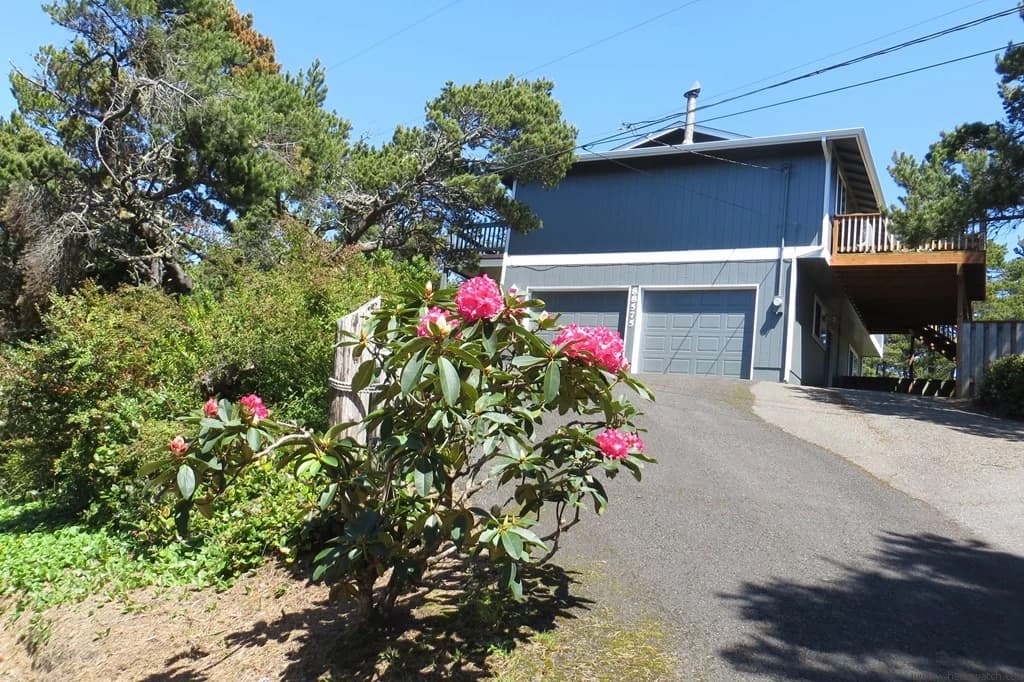 Blue-gray Florence house with a two-car garage, upper deck, and blooming pink rhododendrons