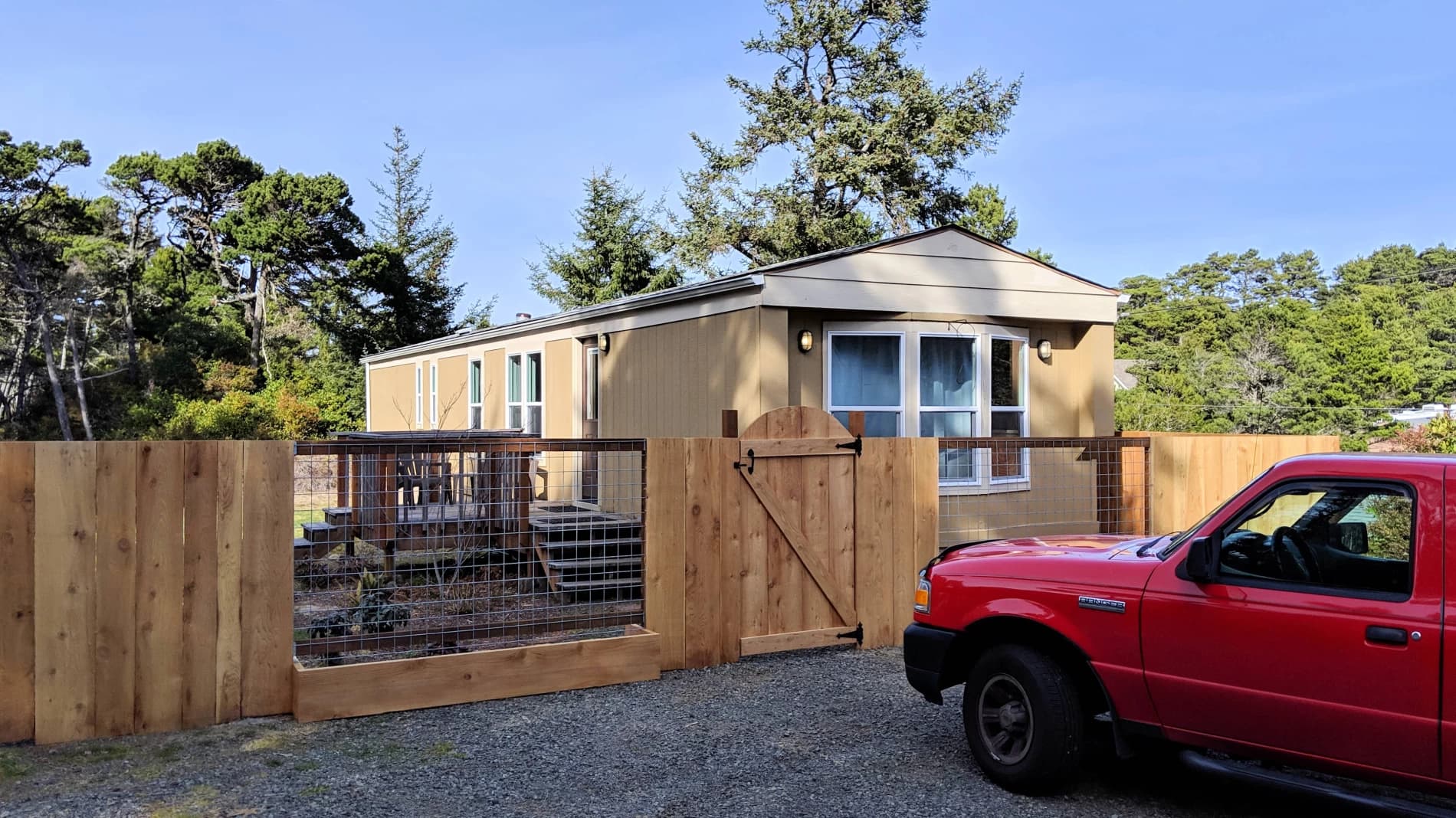 Tan Florence home with a bay window, wood-and-wire fence, and evergreen trees behind