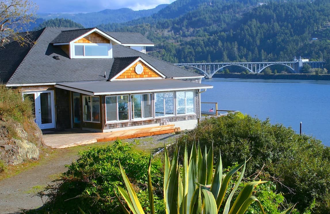 Waterfront house in Gold Beach with a sunroom and deck facing the river and arched bridge