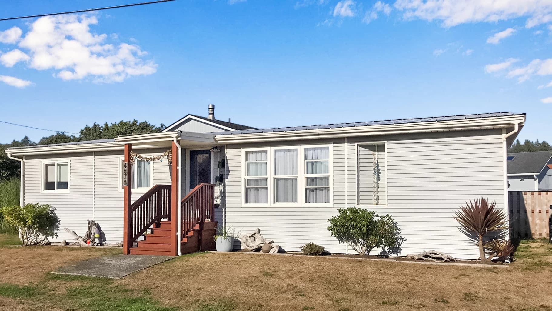 Gray Moclips cottage with brown porch stairs, a dark door, and driftwood by the lawn