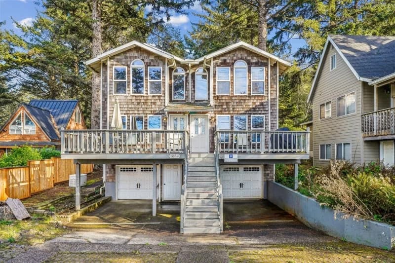 Cedar-shingle Cannon Beach house with arched windows, a wide deck, and garage doors