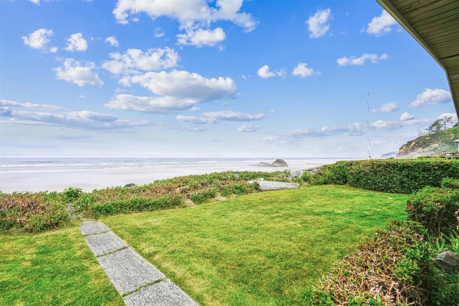 Green lawn in Arch Cape with a stone path leading to sandy beach and ocean