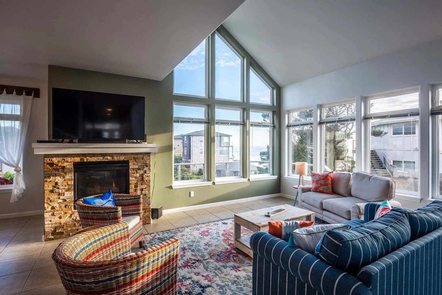 Living room in Gleneden Beach with vaulted ocean windows, a stone fireplace, and striped chairs