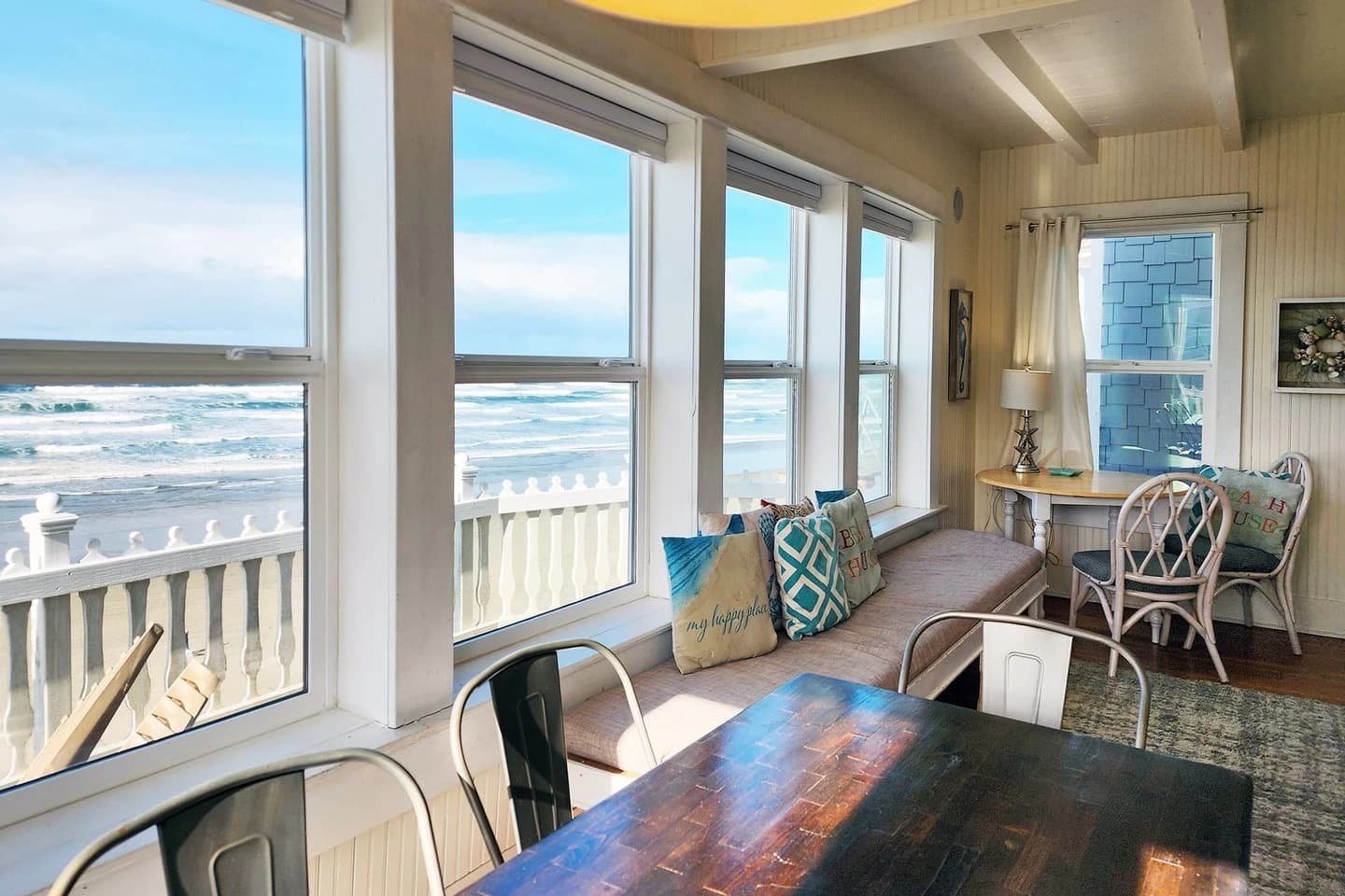 Dining room in Newport with a wood table, window seat, and ocean beyond a picket fence
