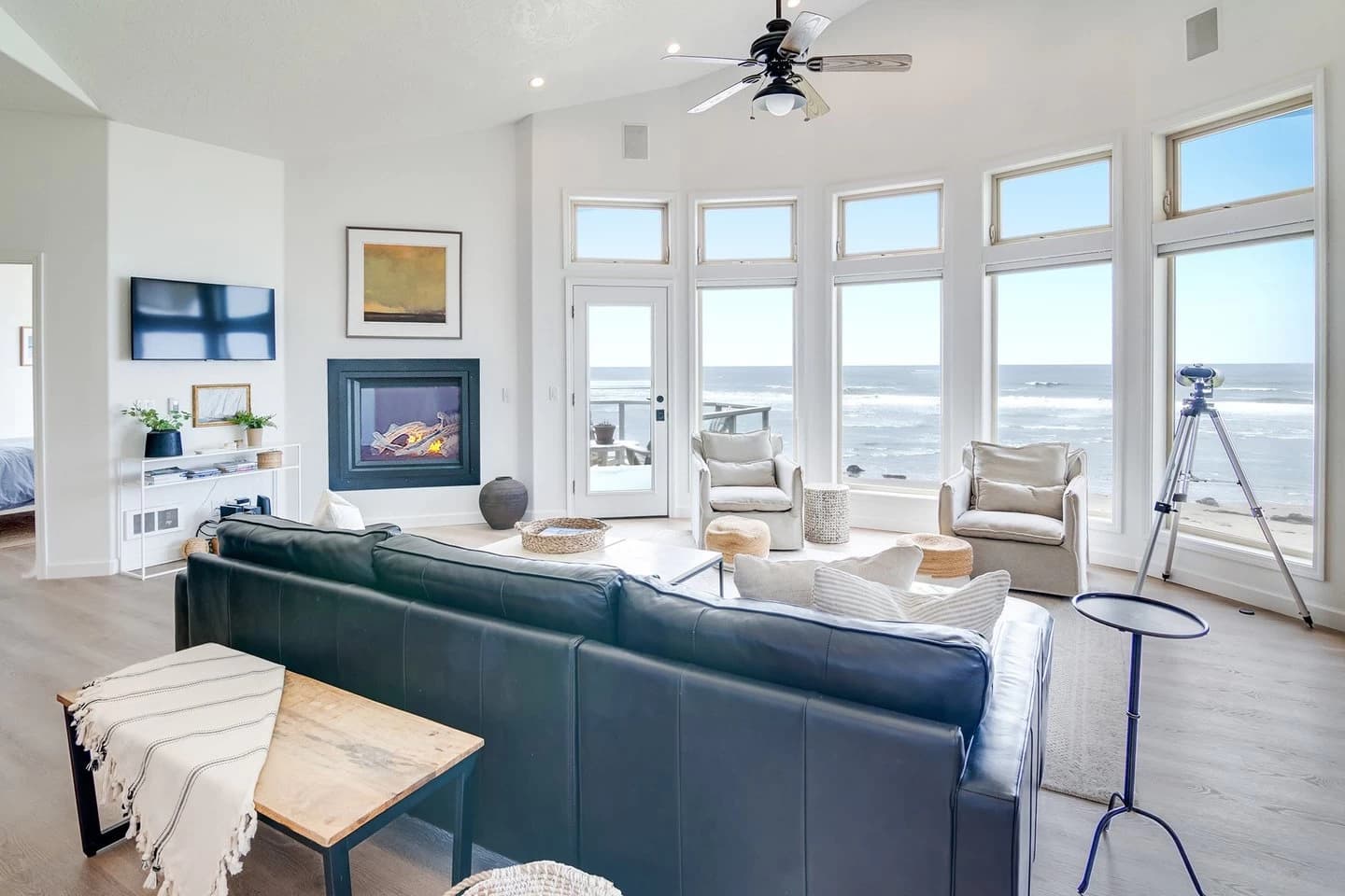 Living room in Seal Rock with beige chairs, a dark sofa, and ocean through tall windows