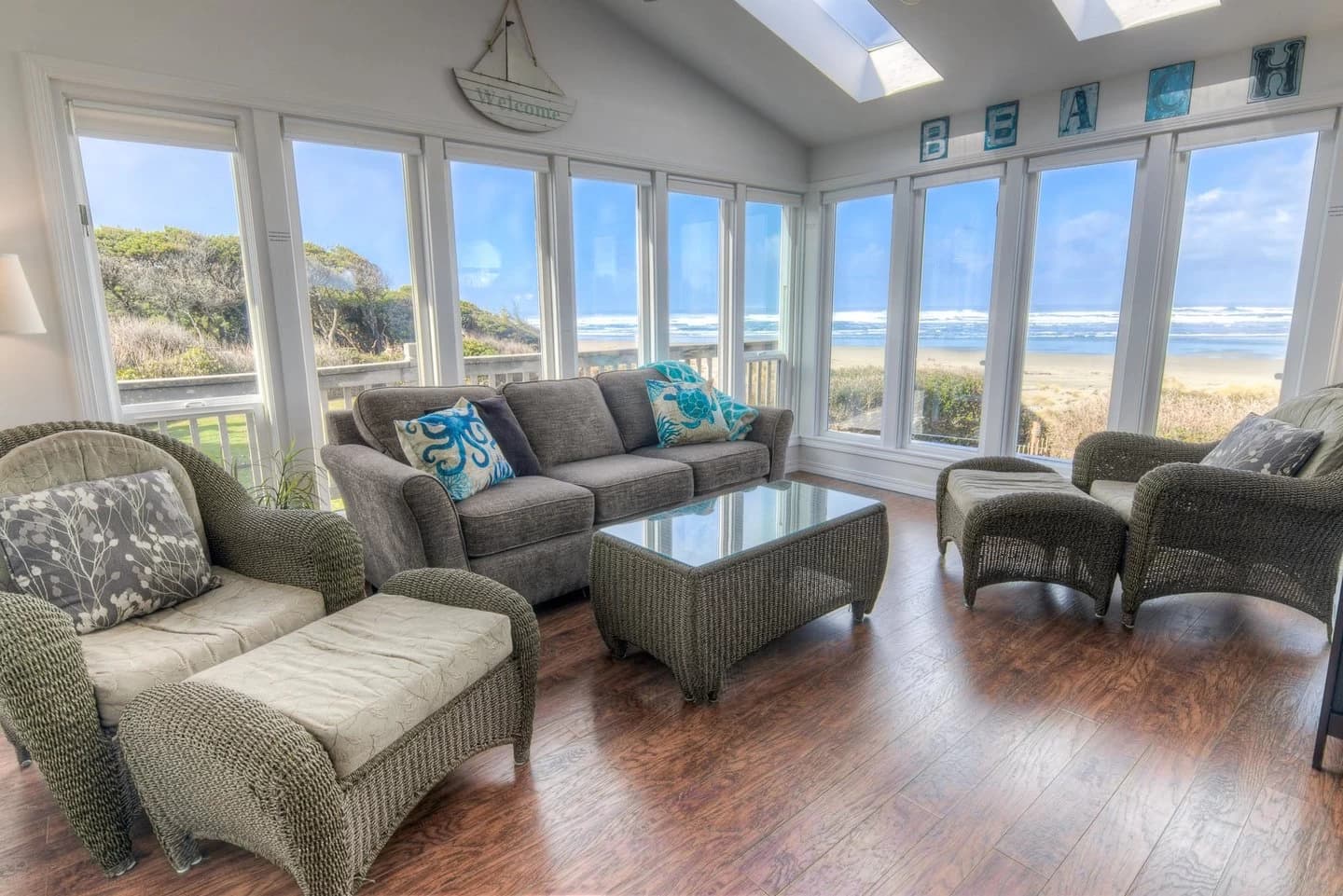 Waldport sunroom with a gray sofa, wicker chairs, and panoramic windows to the ocean