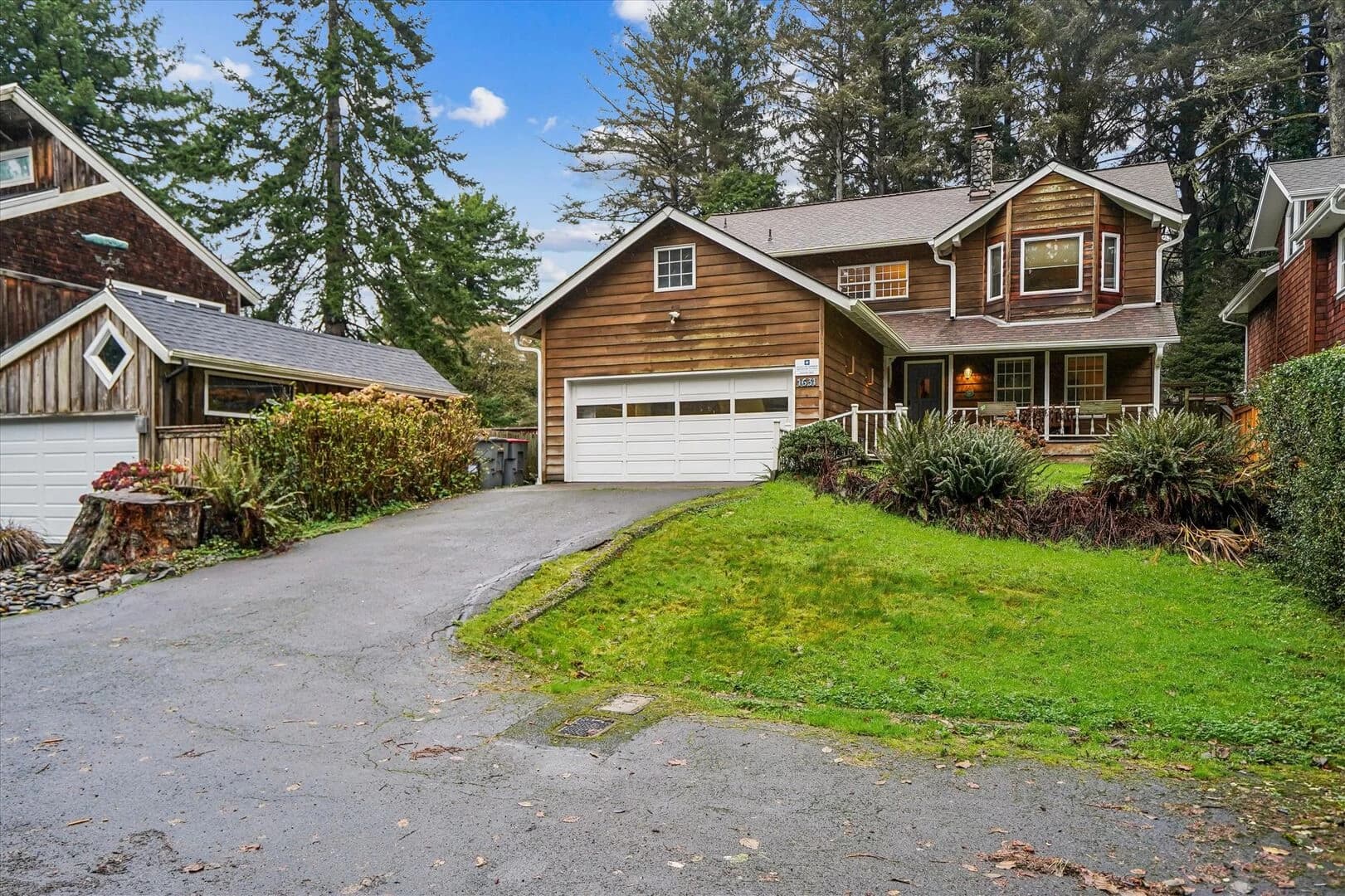 Brown wood-sided house in Cannon Beach with a white garage door amid tall evergreens