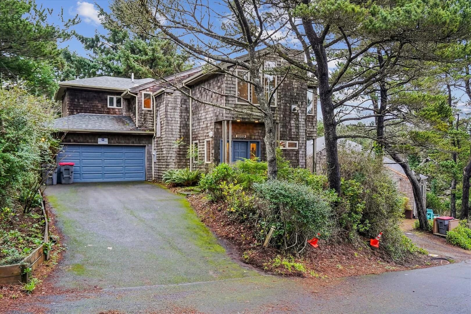 Cedar-shingle house in Cannon Beach with a blue garage door among pines and ferns