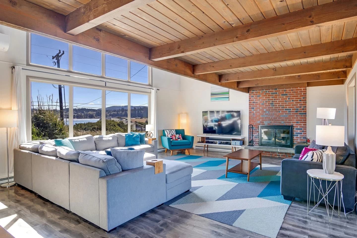 Living room in Waldport with wood beams, a water view, gray sectional, and brick fireplace