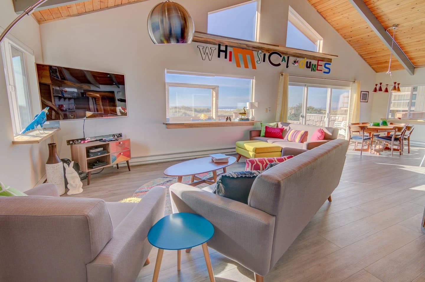 Vaulted Waldport living room with a gray sofa, yellow ottoman, and a beach-view window