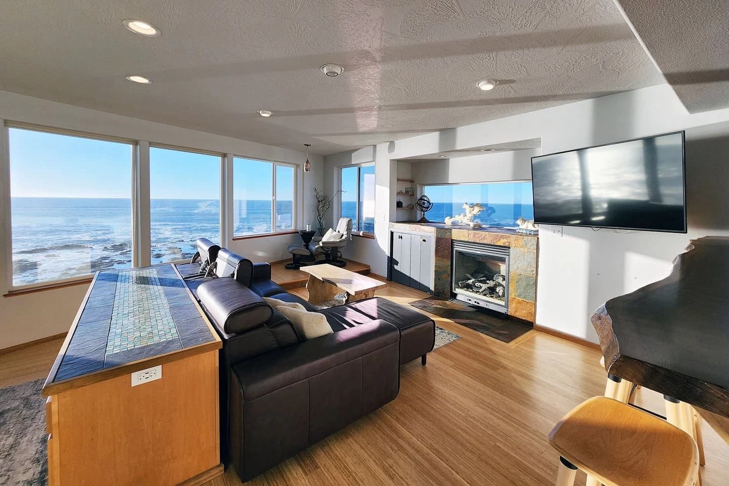 Yachats living room with a leather sofa, stone fireplace, and wall of ocean windows
