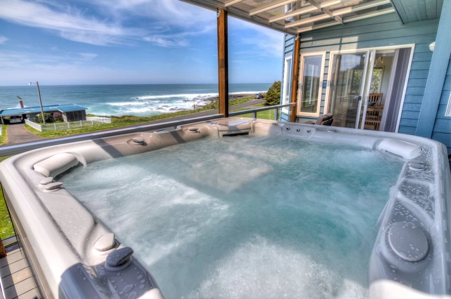 Hot tub on a covered deck in Yachats beside light-blue siding and ocean waves