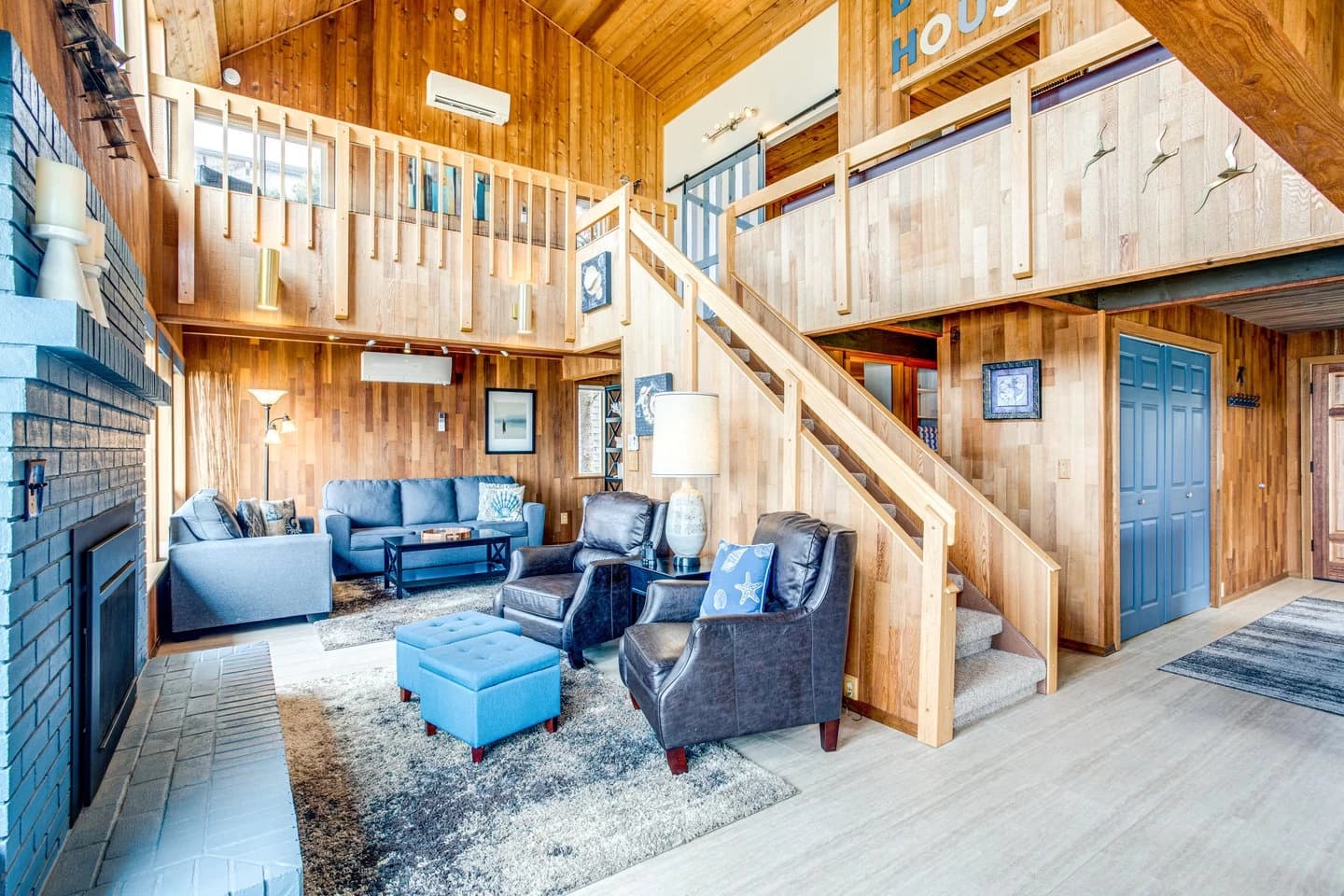 Wood-paneled living room in Yachats with blue sofas, a loft railing, and fireplace
