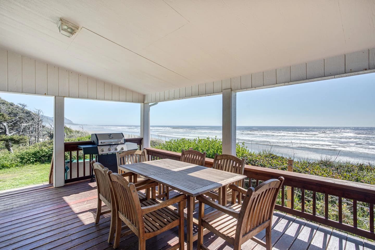 Covered Yachats deck with a wooden dining table, grill, and sandy beach ocean view