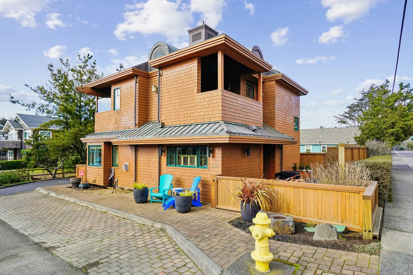 Cedar-shingle Cannon Beach house with teal Adirondack chairs on a brick patio