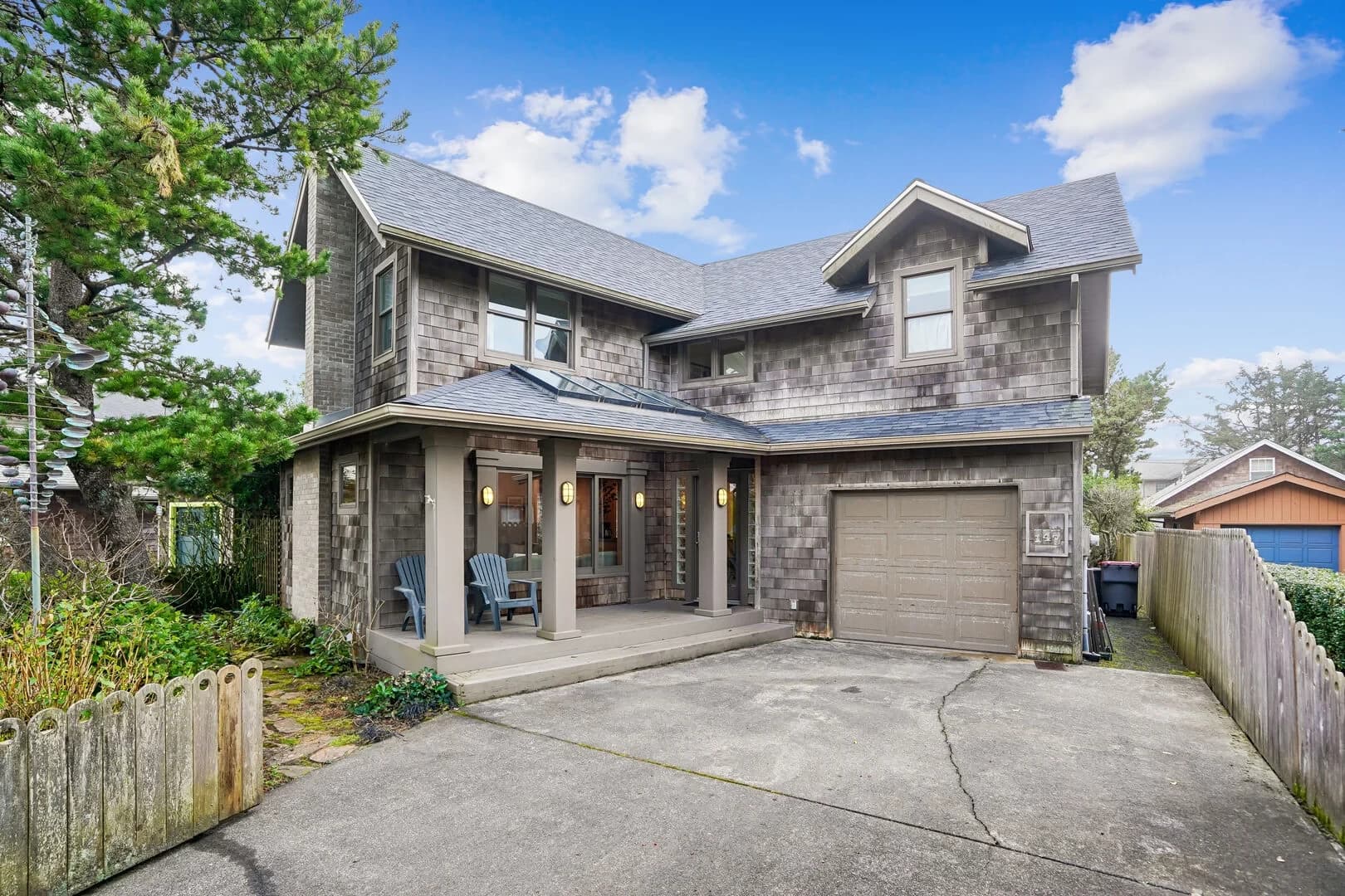 Gray-shingle Cannon Beach house with a covered porch, blue chairs, and garage