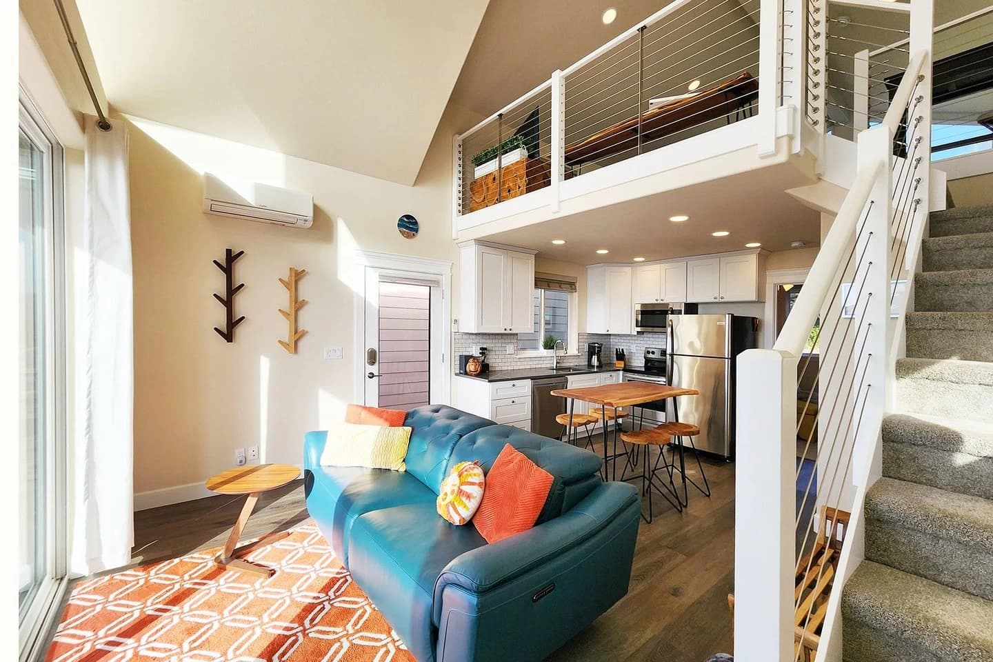 Yachats loft living room with a teal sofa, orange rug, and open white kitchen