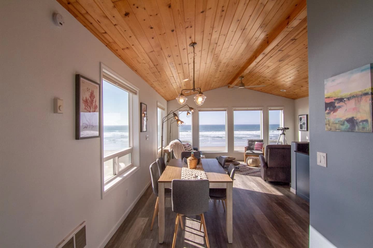 Wood-vaulted dining area with gray chairs faces beach and ocean windows in Waldport