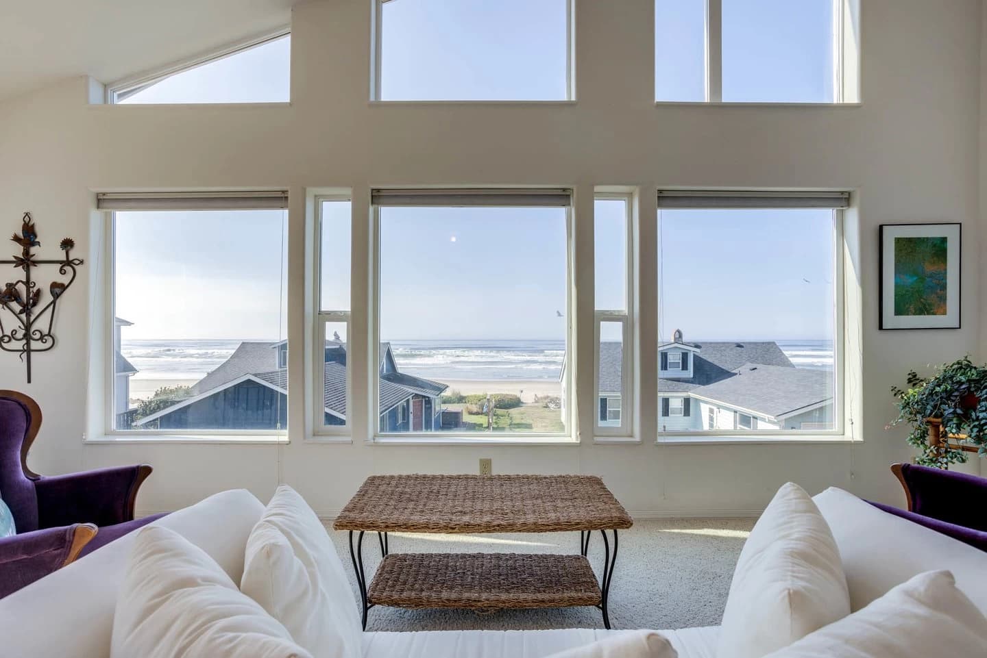 White sofas and wicker table face vaulted ocean windows onto a sandy beach in Yachats